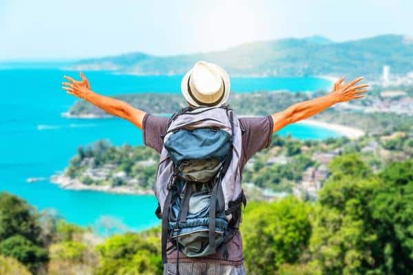 rear view portrait of young man traveler with backpack standing on a mountain with arms spread open travel life style and adventure concept free photo